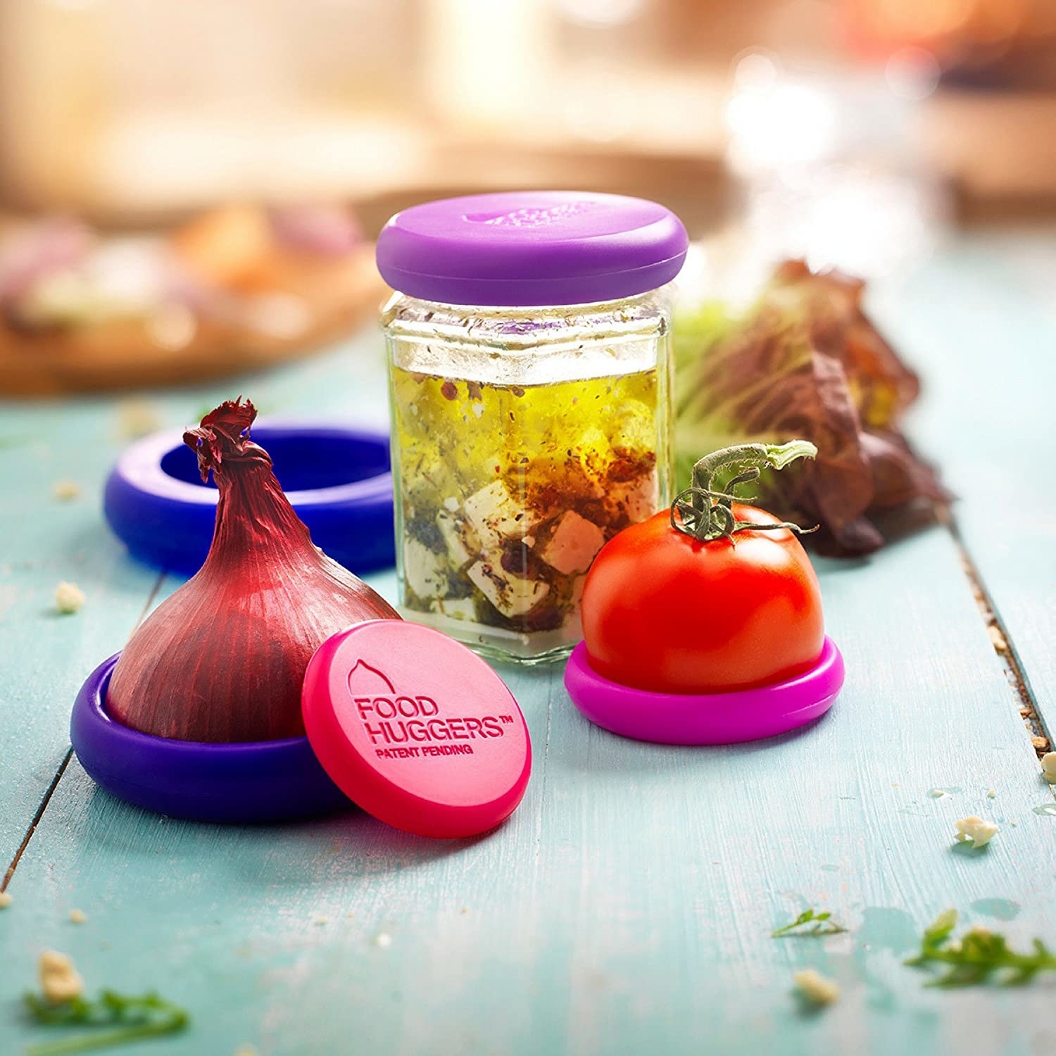 A sliced onion and tomato with silicone lids wrapped around the ends A similar silicone lid is covering a small glass jar