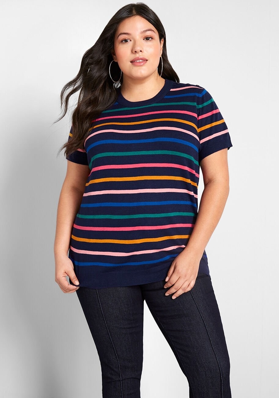 Model wearing sweater in navy blue with multi-colored horizontal stripes