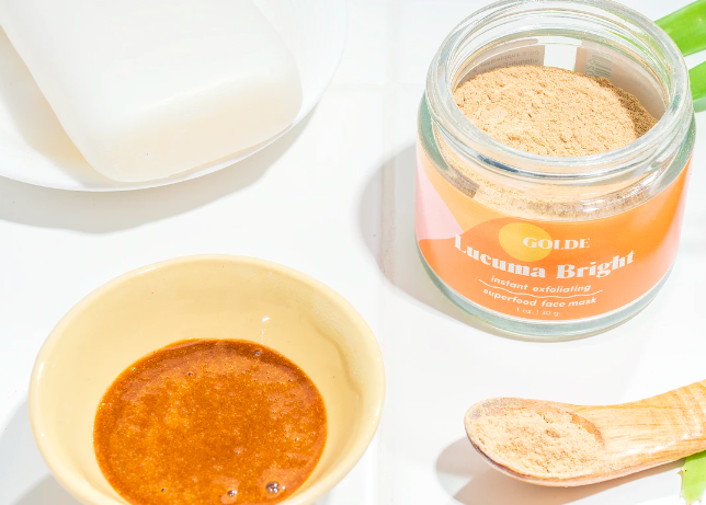 an open container of orange powder next to a bowl of powder mixed with water to create the bright orange mask 