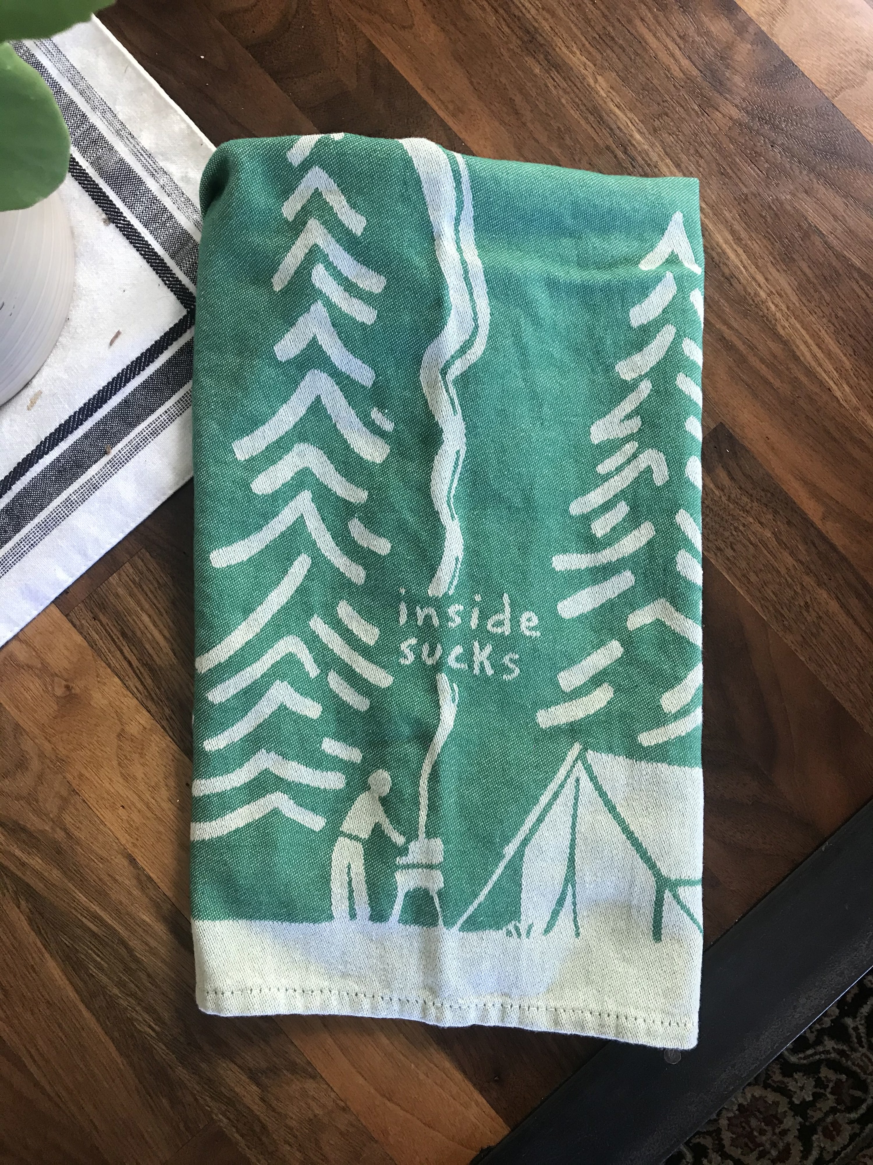 green towel with simple illustration of a tent and someone grilling in the forest reading &quot;inside sucks&quot;