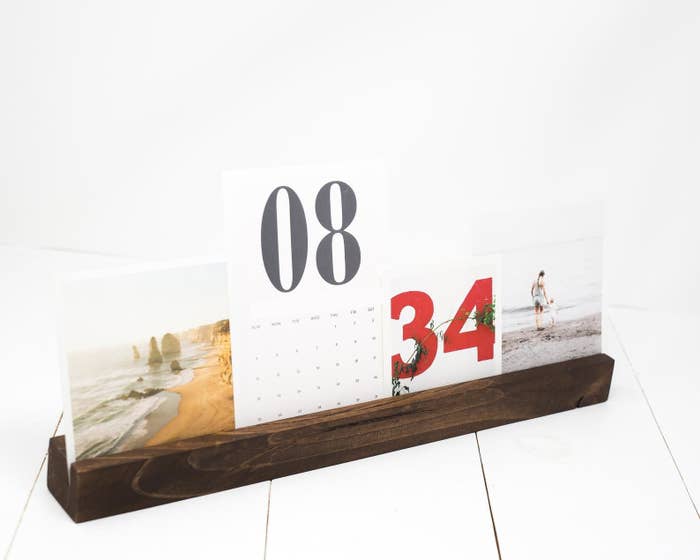A thin rectangular wooden holder with slit down the middle with assorted pictures and a calendar in it