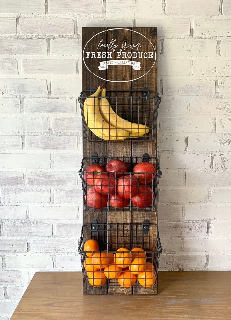 Wall hang with three pieces of wood with three baskets attached and filled with fruit and a circular design at the top that reads &quot;locally sorced fresh produce; hand picked daily&quot;