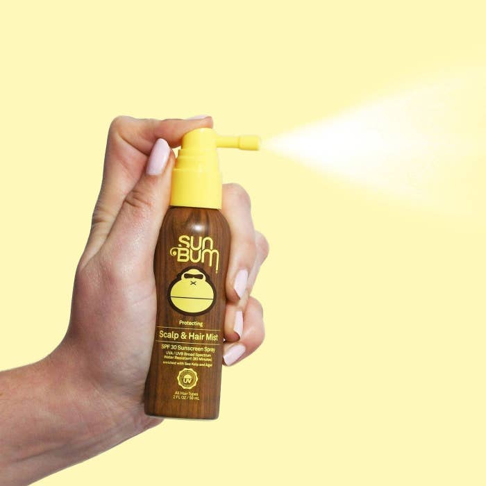 A hand spraying the bottle of sunscreen