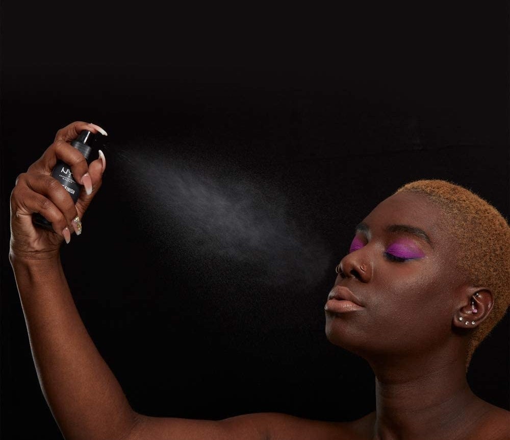 A person spritzes the setting spray onto their fully made-up face