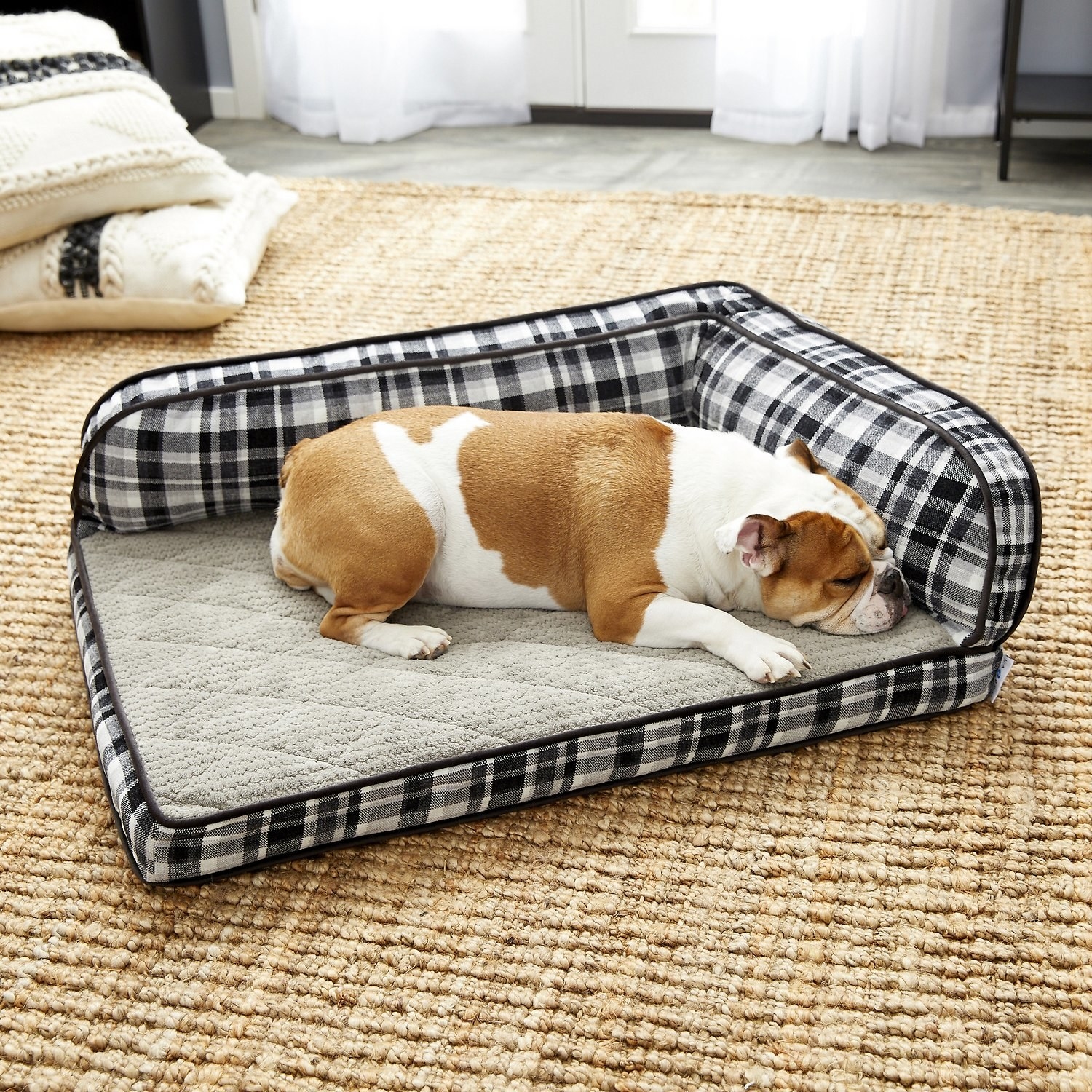 Bulldog laying on the gray dog bed, which has an L-shaped bolster