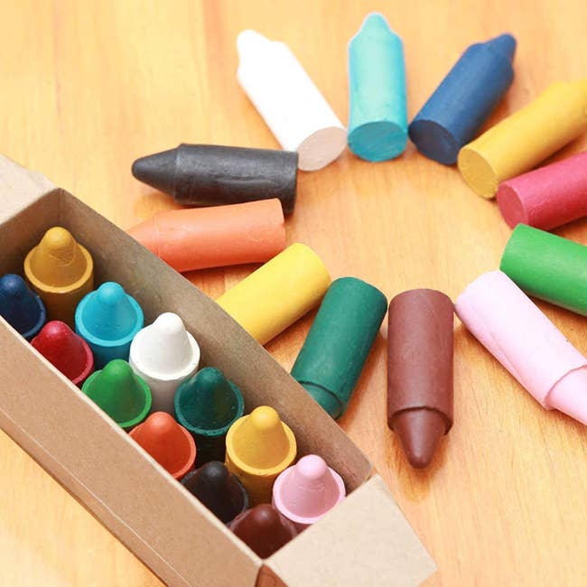 An open box of large, multi-colored crayons with some spread in a circle on a table