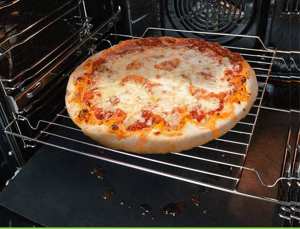 Inside of an oven with a pizza baking and the oven liners sitting on the bottom catching droplets