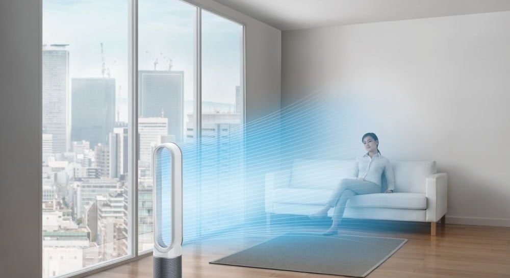 A white and silver Dyson air purifier in a room with a person sitting comfortably on a couch