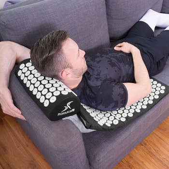 A person laying on top of the mat on their sofa, the mat pillow is raised on the edge of the armrest 