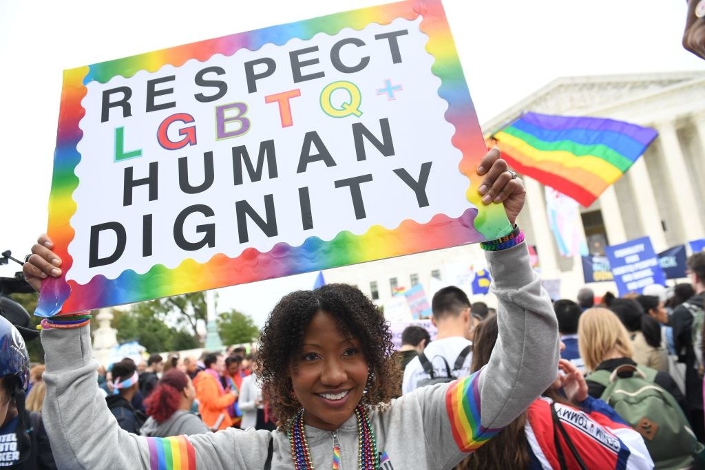 Person holding up rainbow sign that reads, &quot;Respect LGBTQ+ Human Dignity&quot;