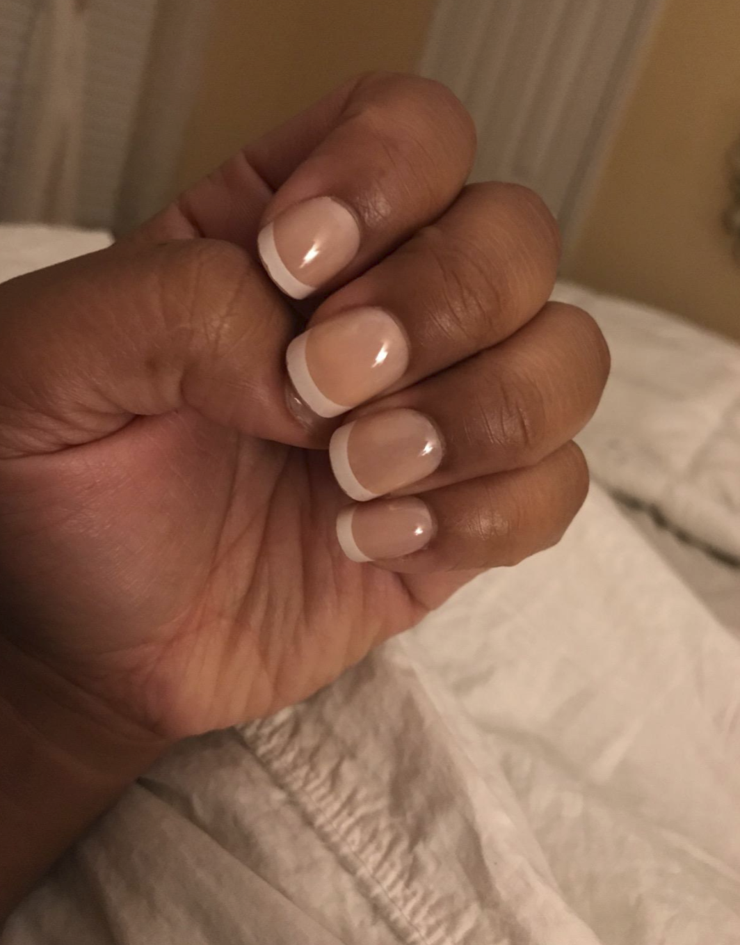 A reviewer&#x27;s hand wearing short press-ons with a French tip style (which are nude with a white line along the end of each nail)