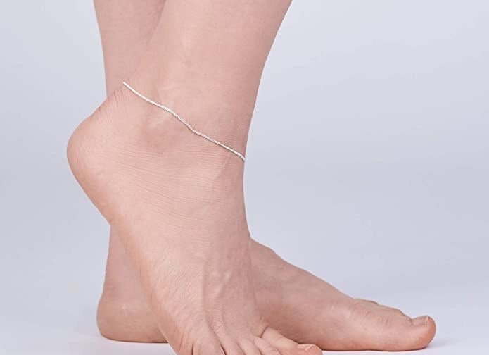 Two feet, one of which has a thin silver anklet
