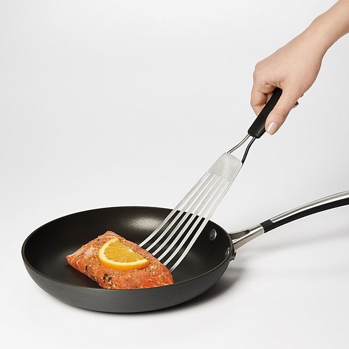 Someone flipping a piece of salmon in a skillet with the fish spatula.