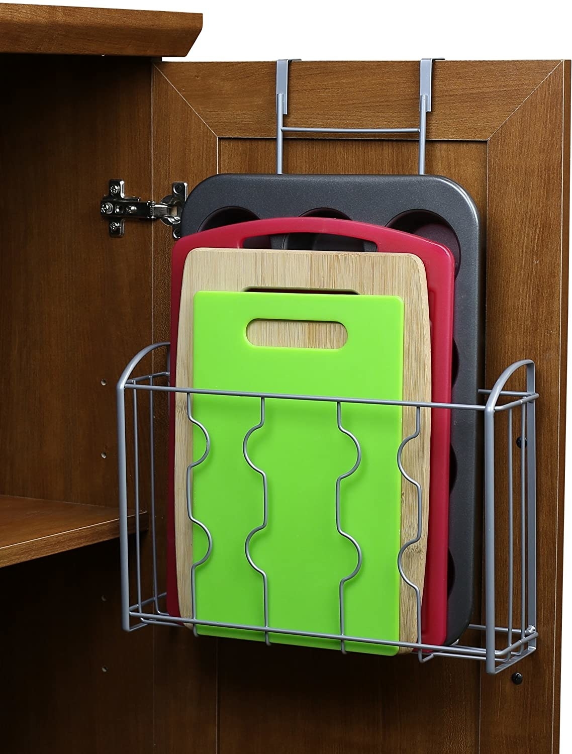 The cabinet organizer hooked onto the back of a cupboard door, holding cutting boards and a muffin tin