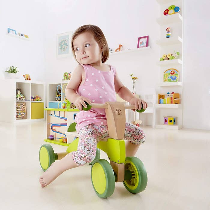 Model child riding a wooden scooter bike with lime green accents on wheels, handle, and base