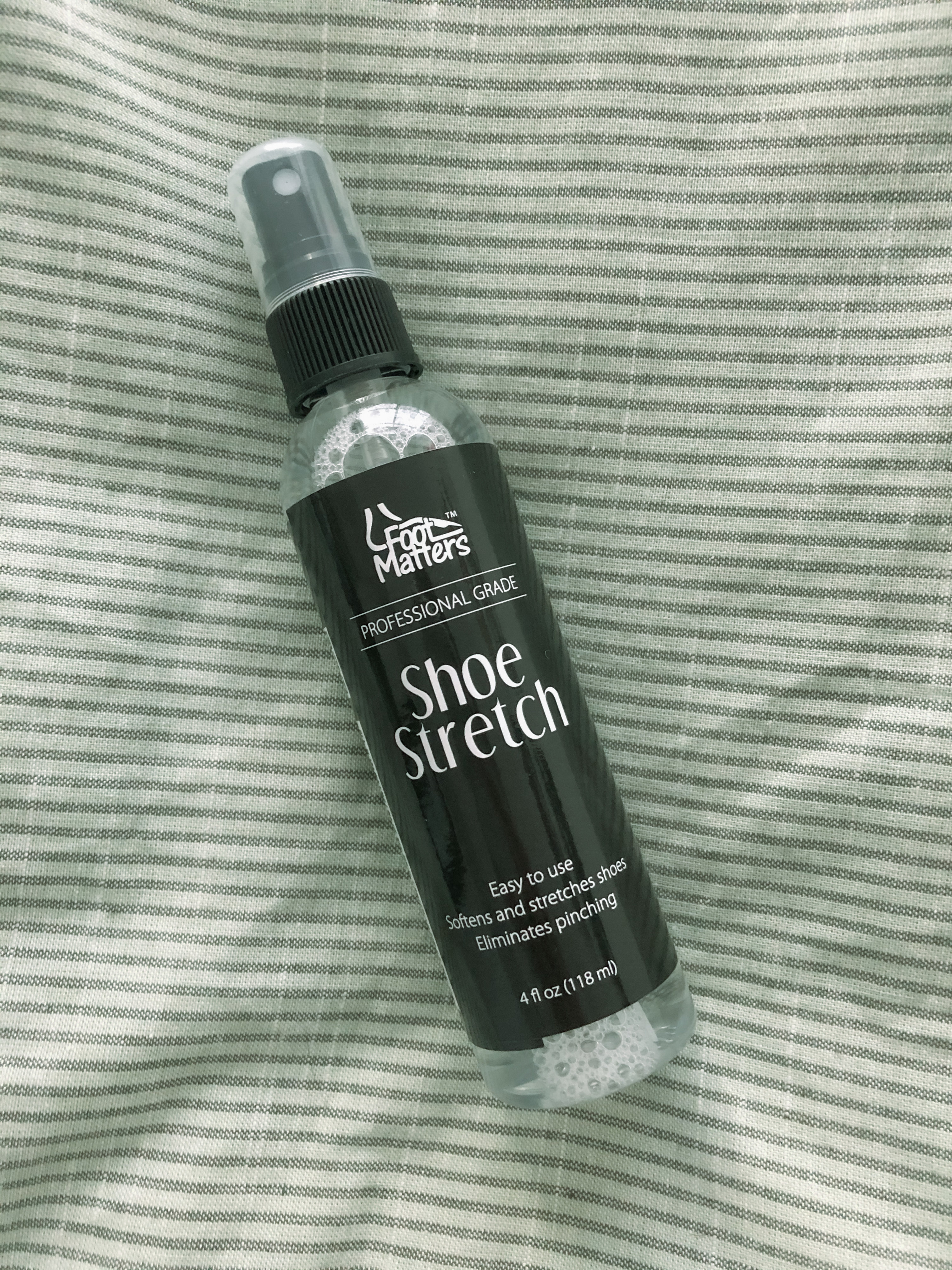 A bottle of the shoe stretch spray is seen on a soft fabric background