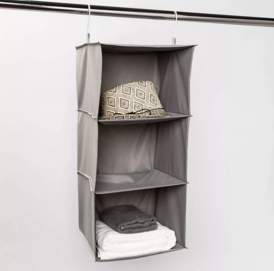 Gray three-shelf hanging organizer with a patterned fedora and folded towels