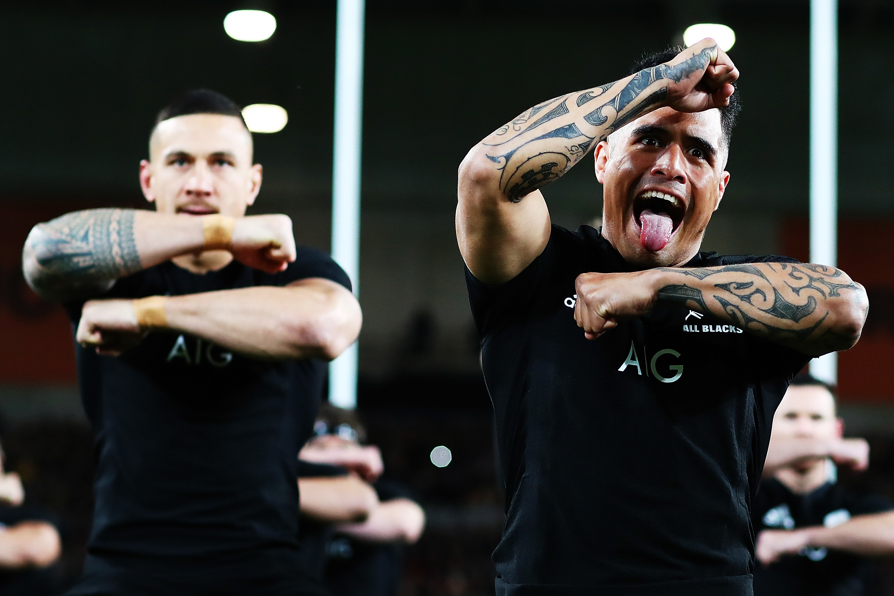 Two members of the New Zealand All Blacks rugby team pulling intimidating faces while doing the haka