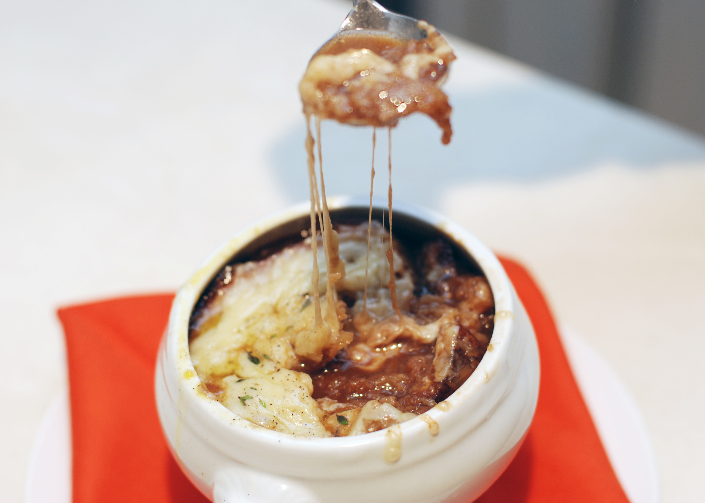 A spoon taking a bite of Balthazar copycat French onion soup from a bowl with a thick layer of cheese on top.