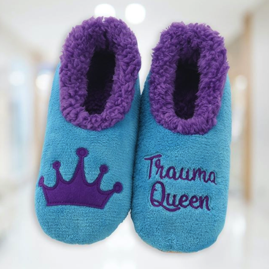 A pair of embroidered, fuzzy slippers. One has a crown on it and the other reads &quot;Trauma Queen.&quot;