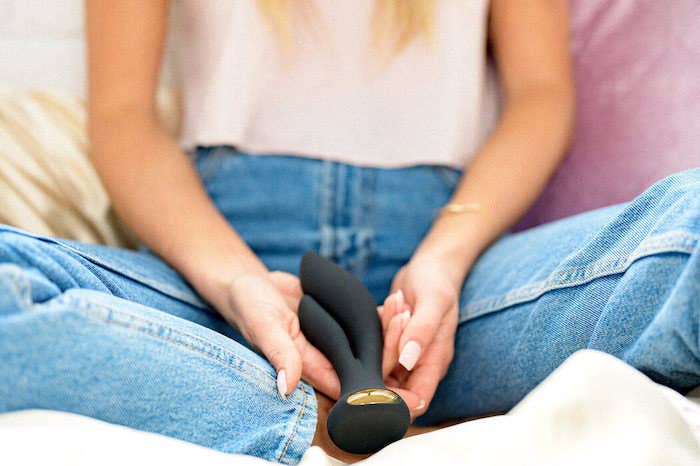 A woman holding a two-pronged rabbit-style vibrator between her legs.