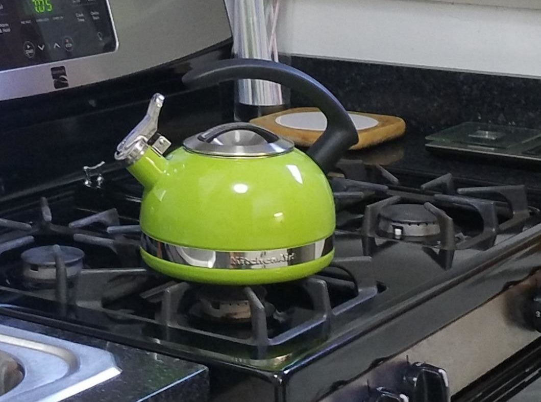 An apple green teak kettle with a black handle and silver accents and top sitting on a stovetop