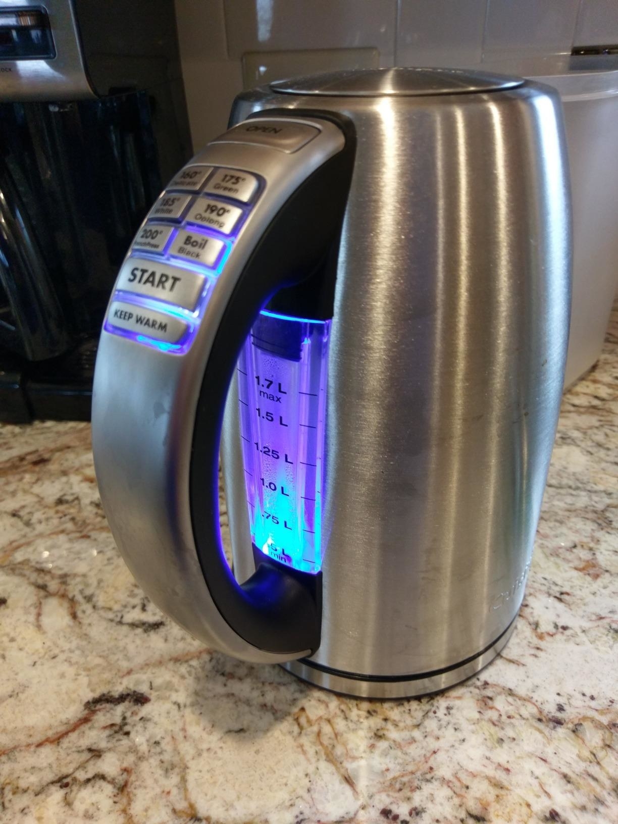 A metallic electric tea kettle with temperature buttons and measurements illuminated in blue light 