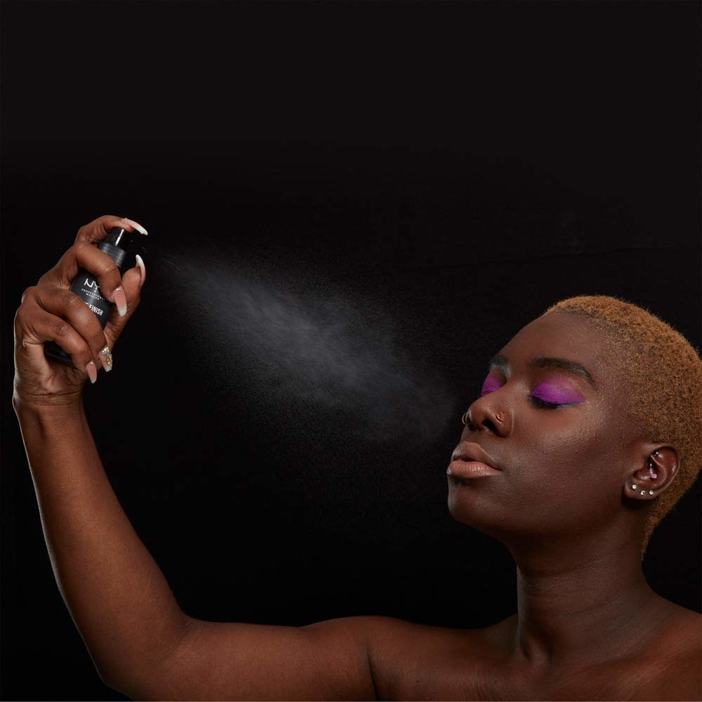 A model spraying the setting spray on their face, which has colorful eye makeup 