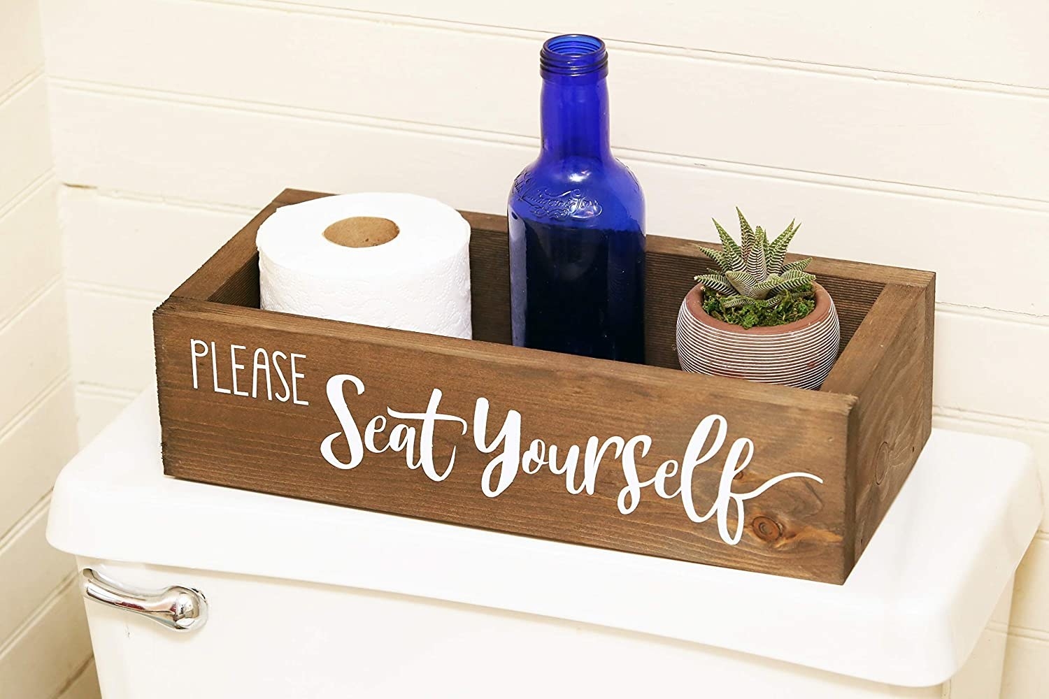 A wooden box placed neatly on top of a toilet that reads &quot;Please Seat Yourself.&quot;