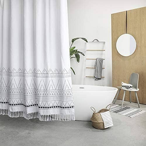 The fabric shower curtain with a triangle design across the bottom third and fringe across the bottom hanging around a bathtub.