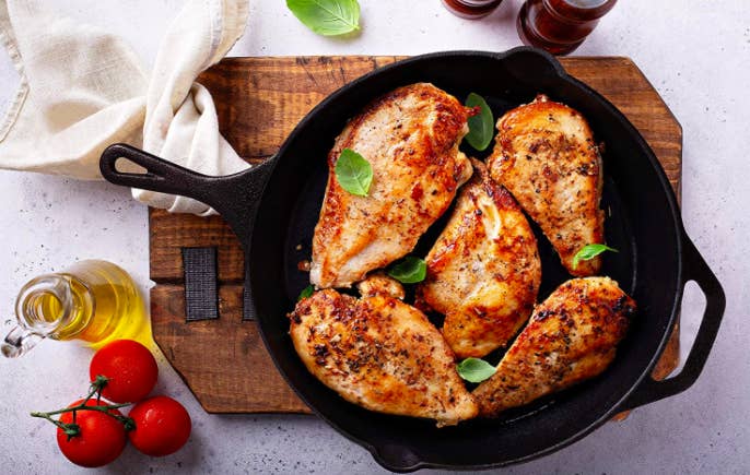 A black cast iron skillet filled with grilled chicken breasts and basil leaves