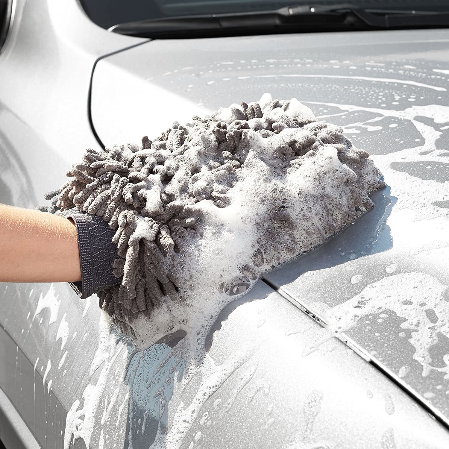 A person scrubbing the hood of their car with the washing mitt