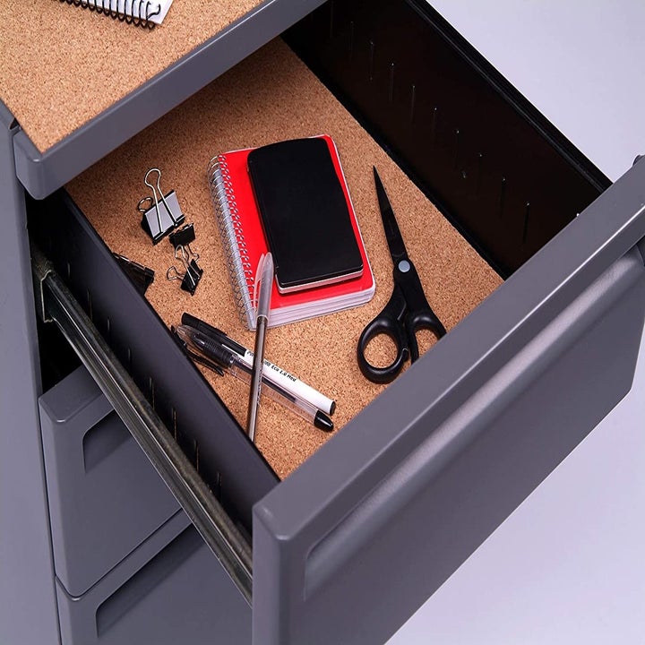 A drawer lined with adhesive cork covering with scissors, notebooks, and pens inside