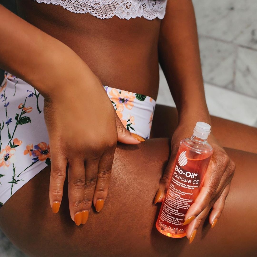 A person putting Bio-Oil on their thigh while wearing a swimsuit