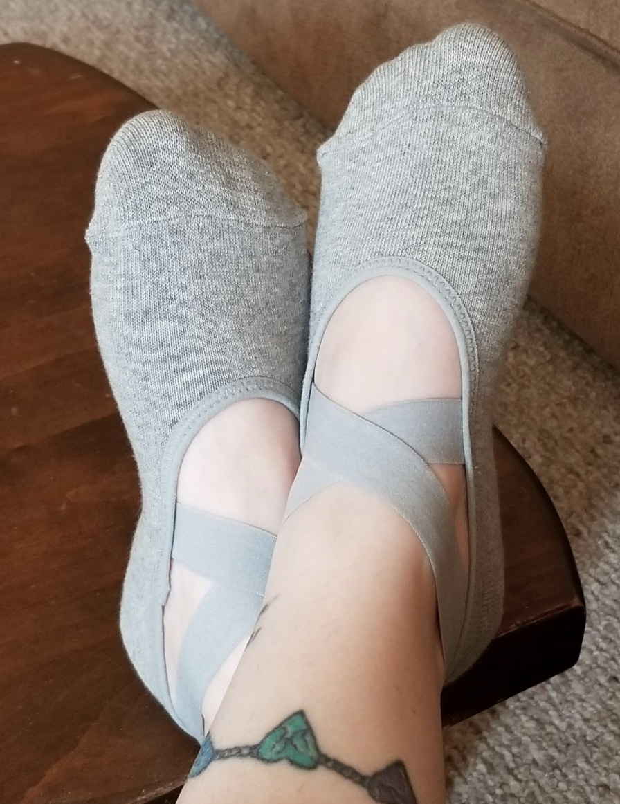 A reviewer image of feet wearing the gray socks with two crossover elastic straps on the top of the foot 