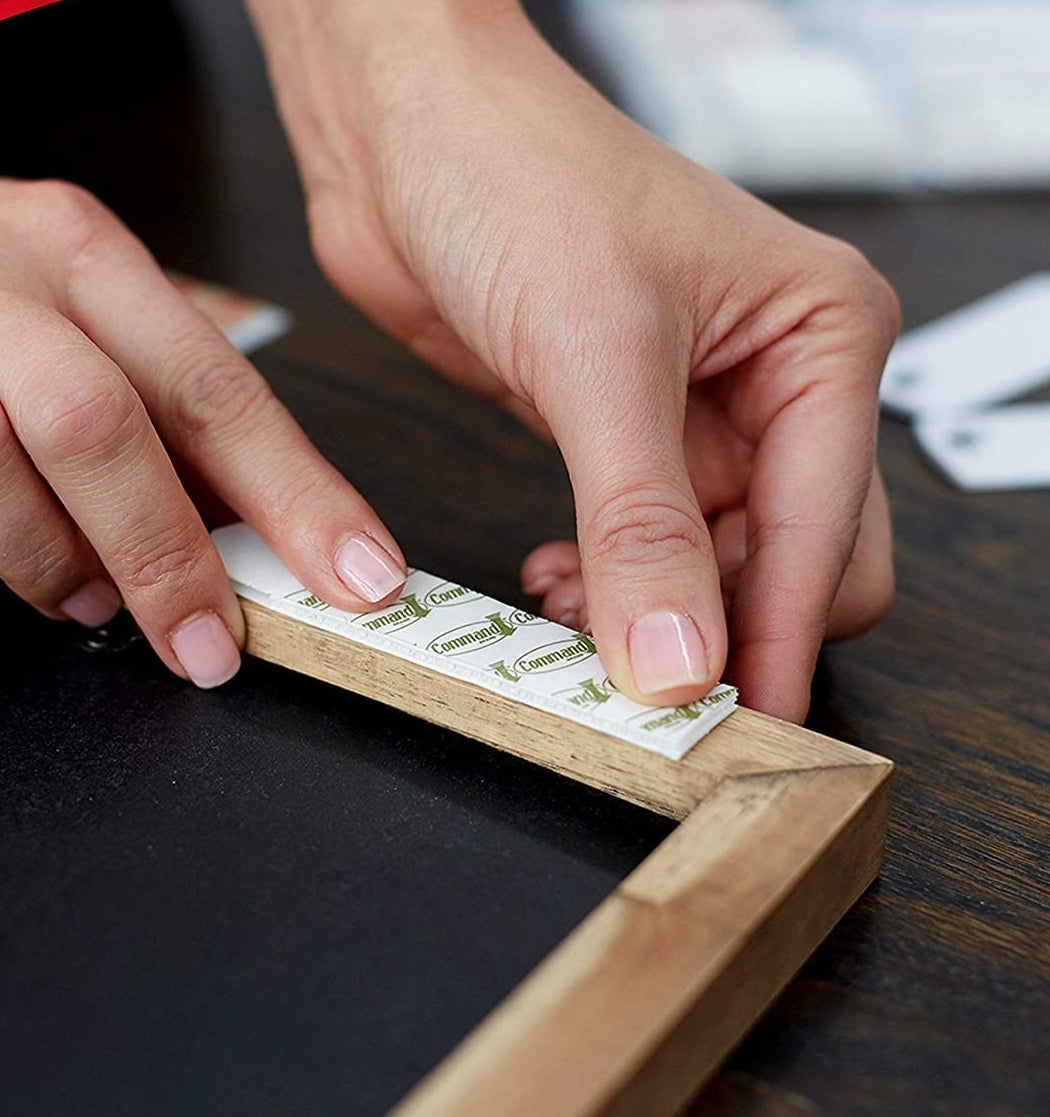 A person putting a Command strip on the back of a frame