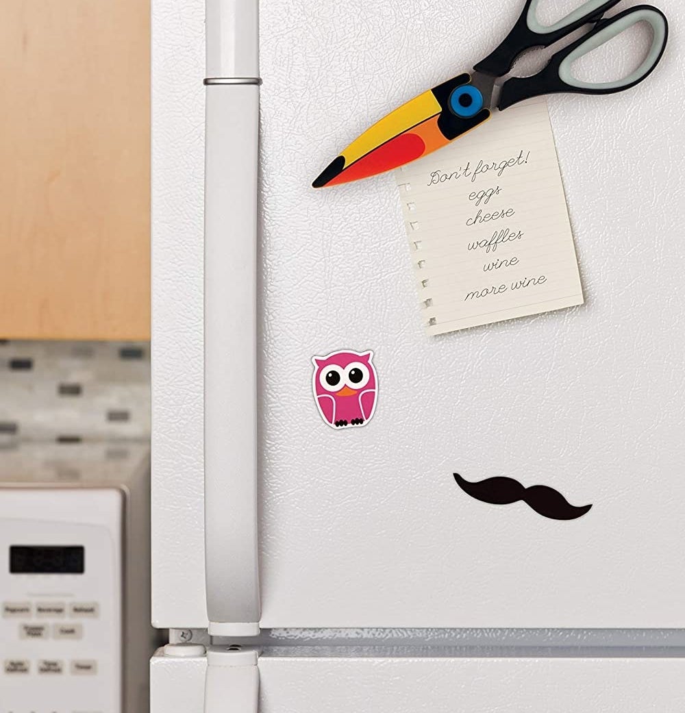 Toucan-shaped scissors are seen attached to a fridge door, holding up a grocery list