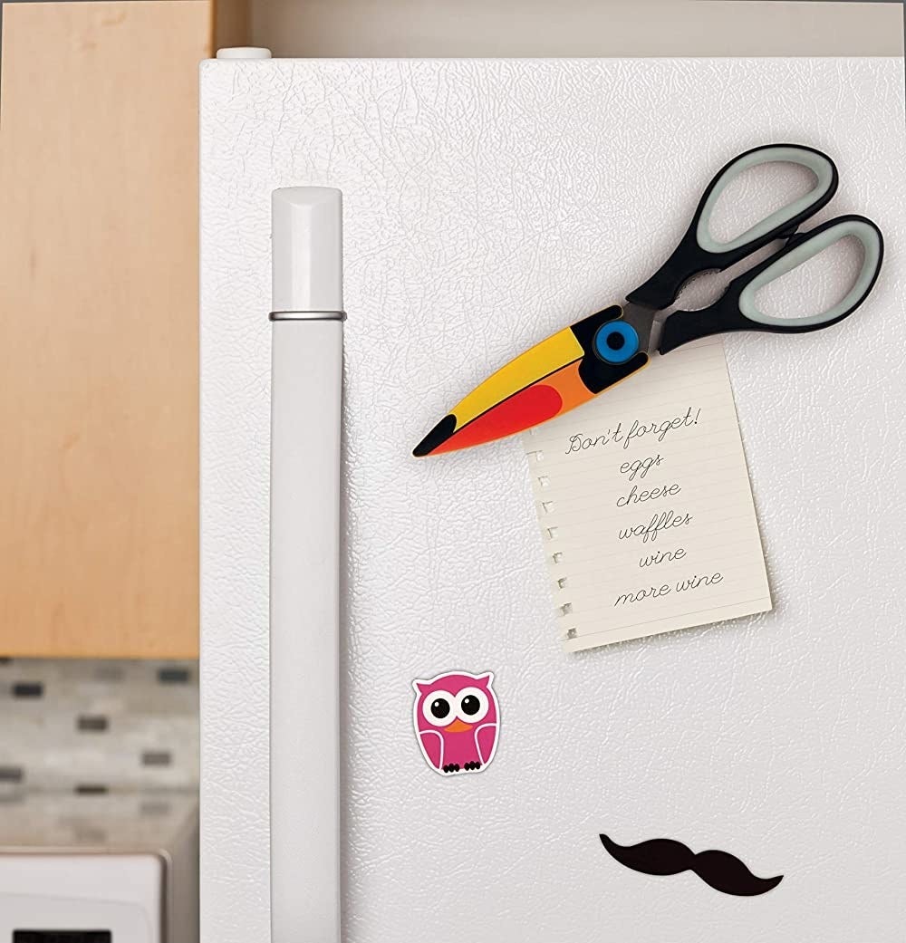 Toucan-shaped scissors are seen attached to a fridge door, holding up a grocery list