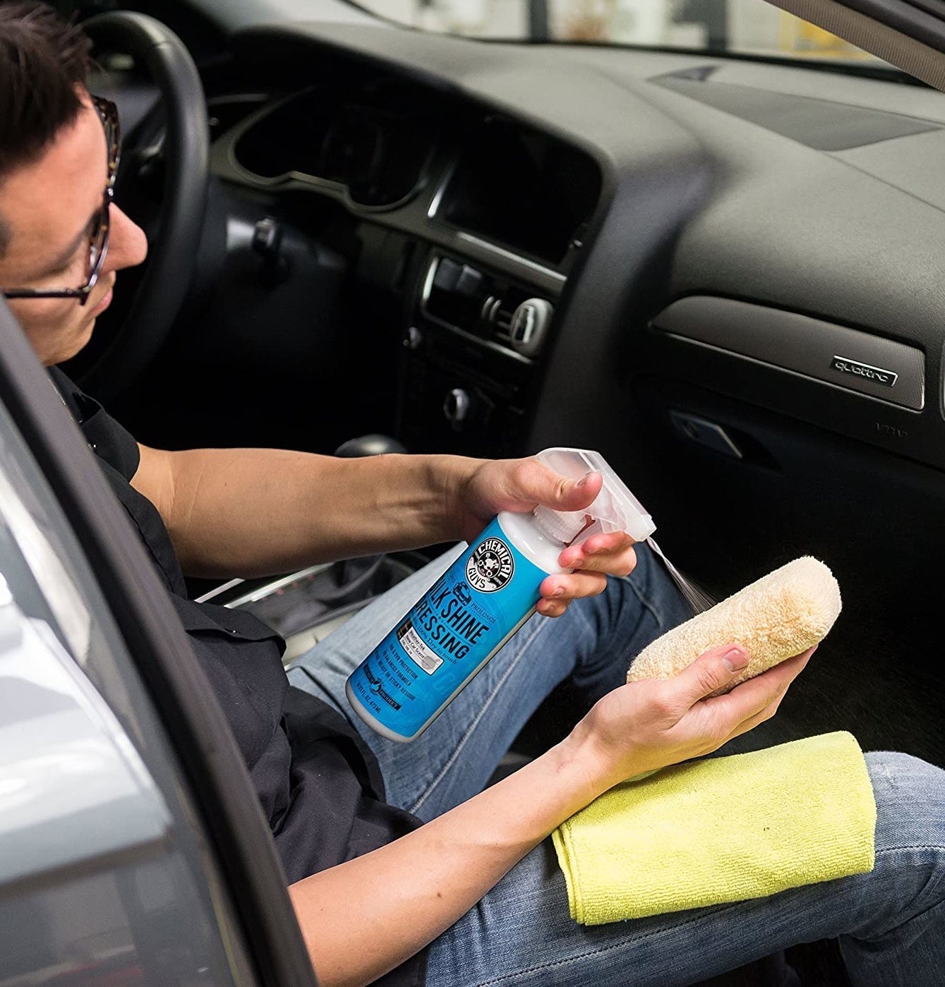 A person sprays the protective spray onto a sponge while sitting in a car