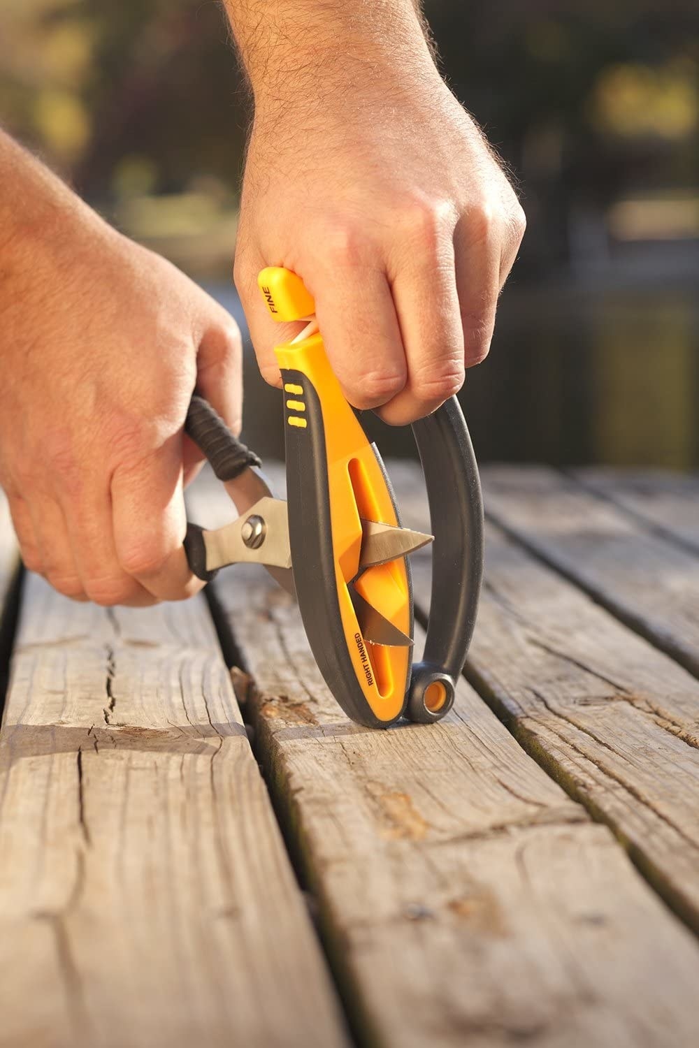 person using the sharpener outdoors to sharpen a pair of scissors