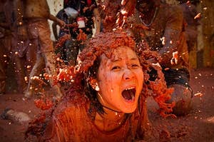 Woman in a crowd absolutely covered in tomatoes (and their juices) at a tomato festival in Spain