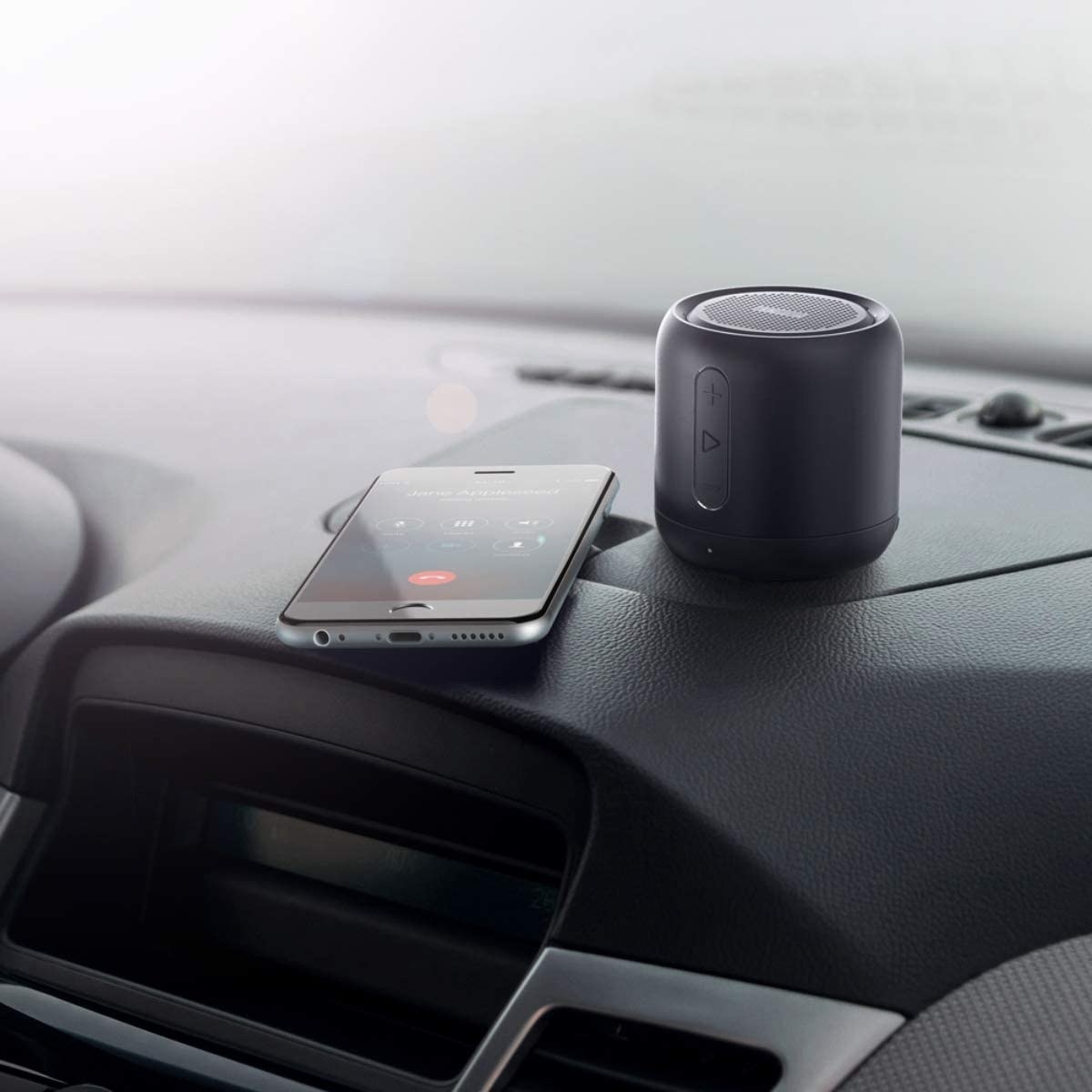 A Bluetooth speaker sitting on a car dashboard next to a phone