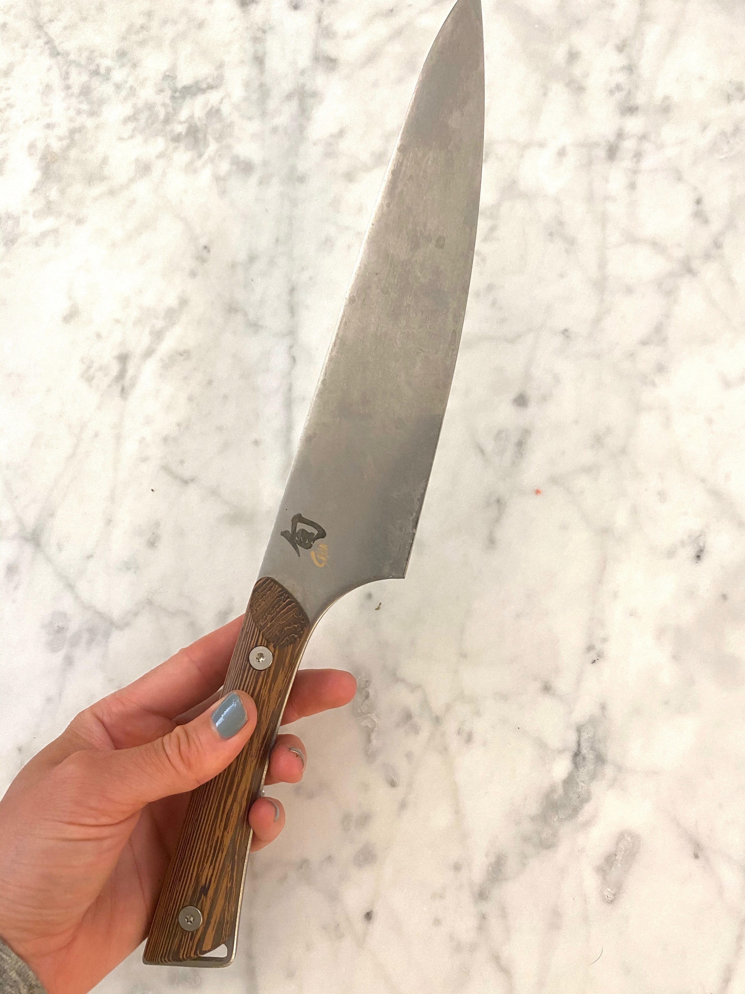 A hand holding a Shun chef&#x27;s knife over a marble background.
