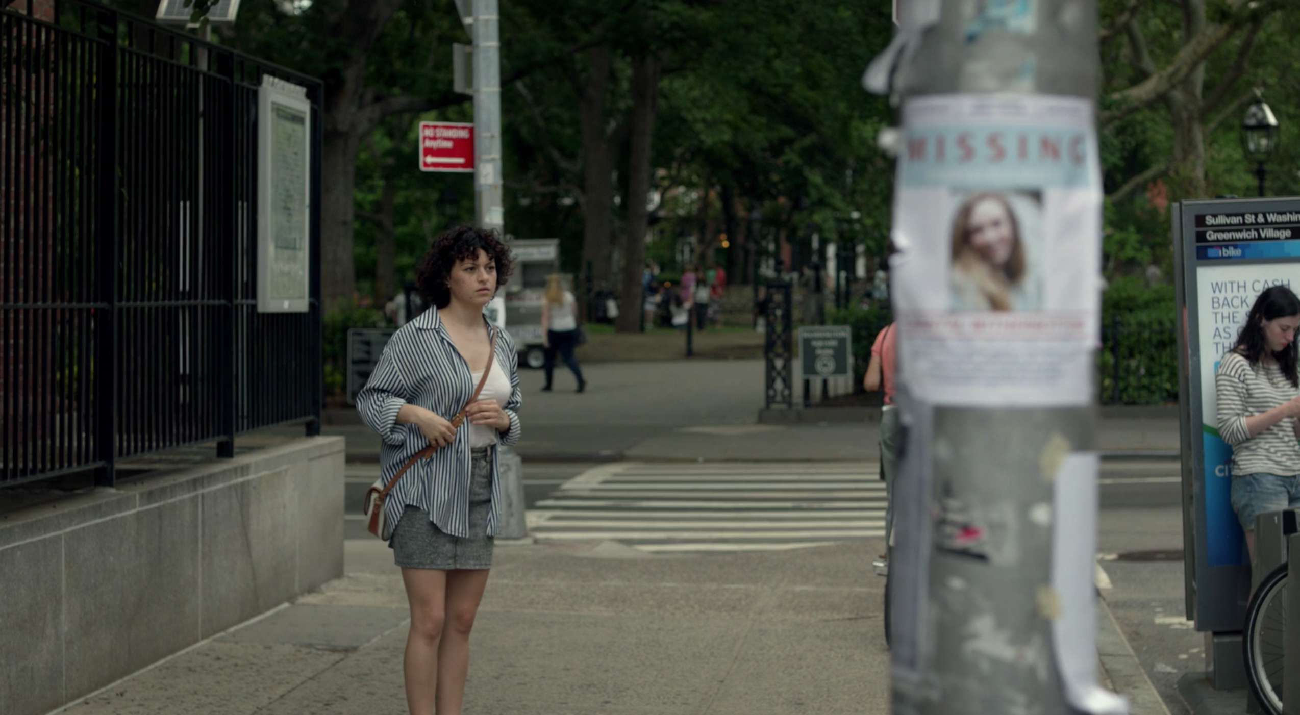 Screenshot of Alia standing in the streets near a missing persons poster