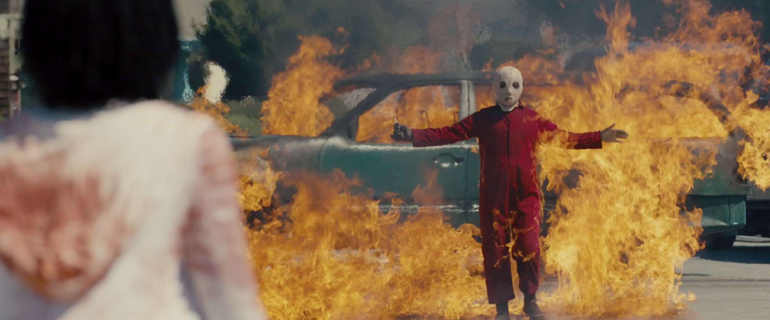 Screenshot of one of the doppelgangers standing in front of a burning car
