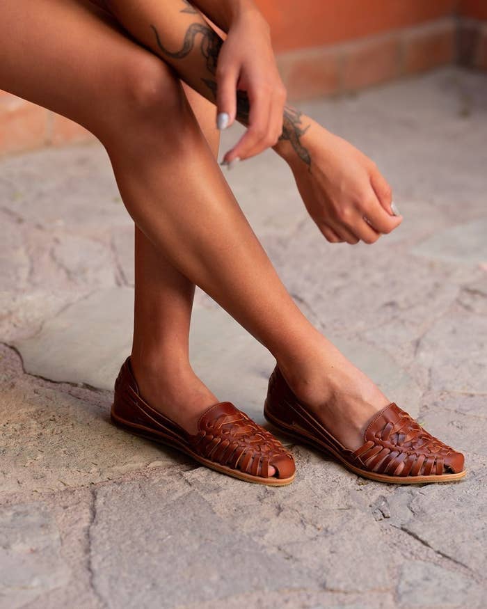 A model wearing the shoes without socks and slightly bending their foot, showing the flexibility of the soles and leather 