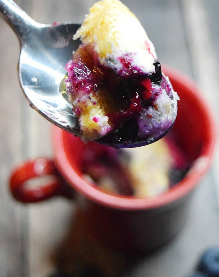 A spoon taking a scoop of blueberry pancakes from a mug.