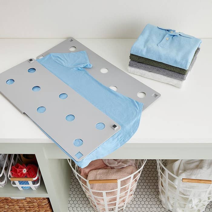 A light gray laundry folder in the process of folding a light blue T-shirt