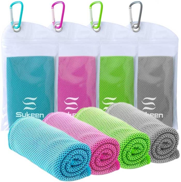 A blue, pink, green, and gray cooling towel rolled up next to their carrying cases, which come with keychains 