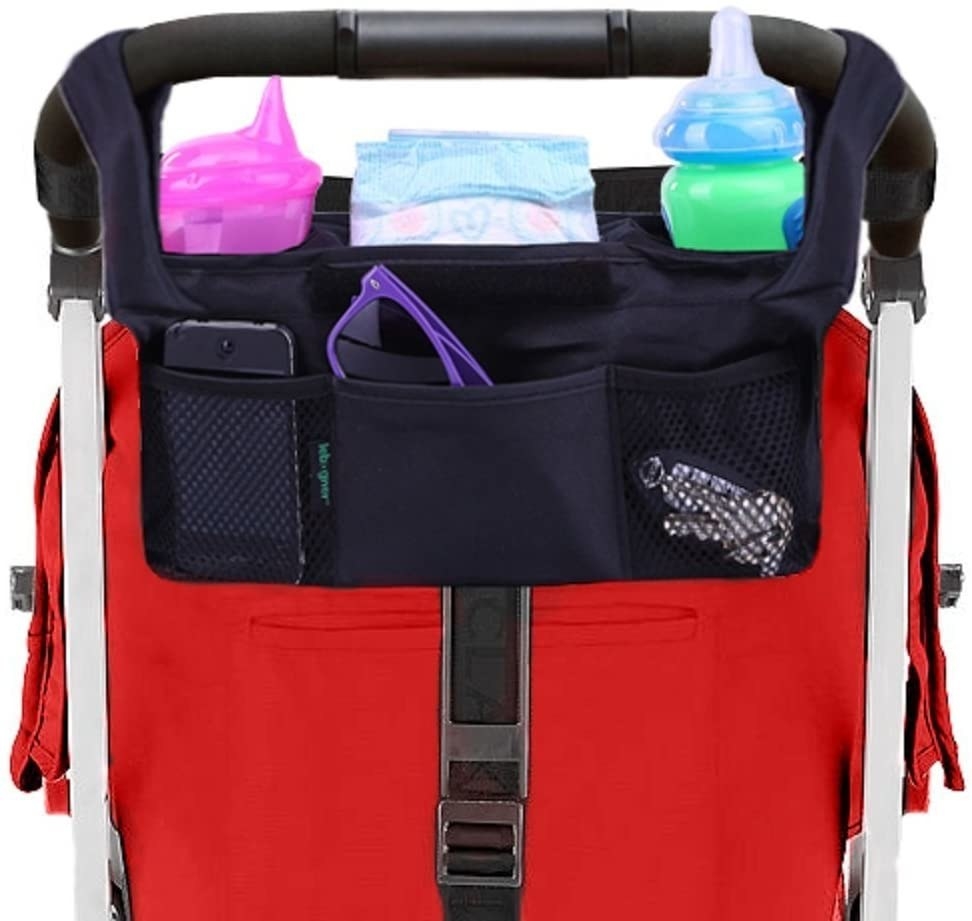 A stroller with a fabric bag hanging from the handles The bag has multiple pockets with items like a cellphone, diaper, keys, and sippy cups in them